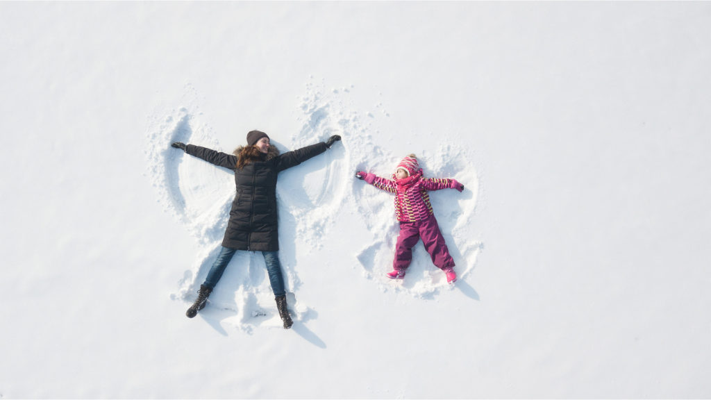 Lapsi ja äiti tekevät lumienkeleitä.
